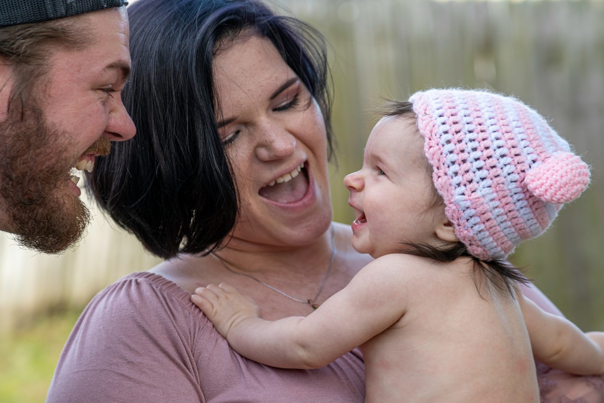 Photo d'une jeune maman avec son tout jeune bébé dans les bras, s'amusant du papa
