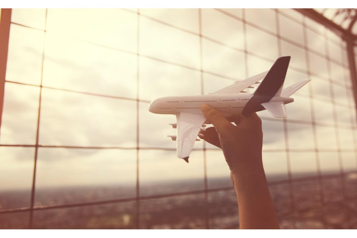Photo d'un avion tenu dans la main d'un jeune enfant, avec un aéroport en toile de fond